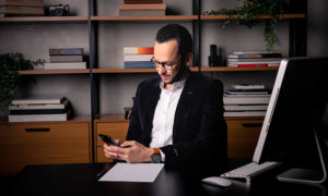 Xerxes Marques usando o celular em sua mesa de trabalho